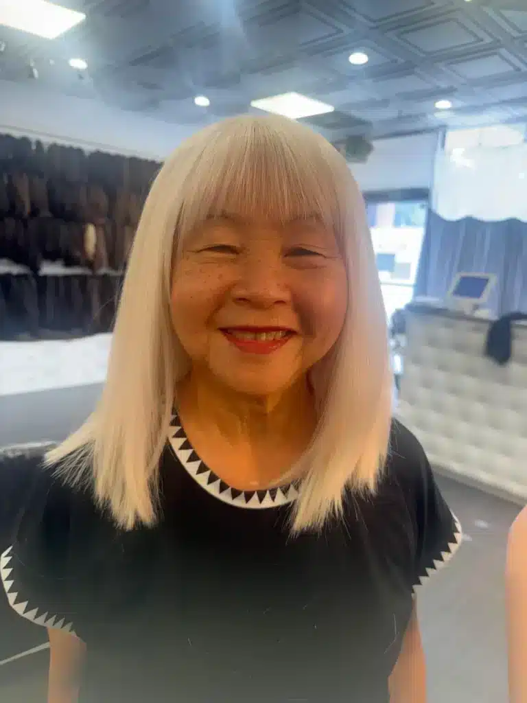 Woman with shoulder-length platinum blonde hair and blunt bangs smiling in a salon.